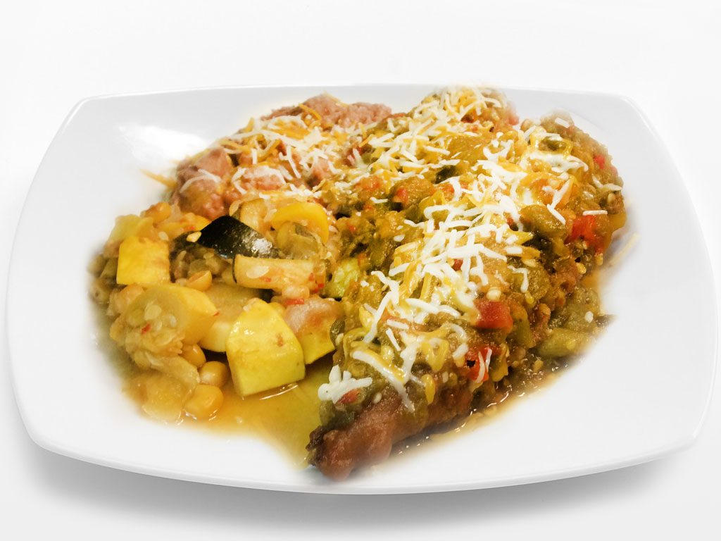 A plate of calabacitas, squash and corn, next to beans under green chile and melted cheese